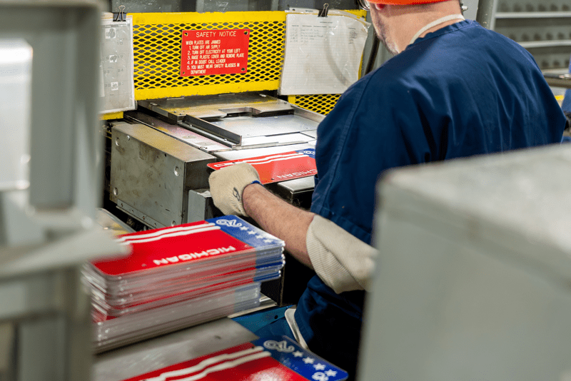 A prisoner operating a metal stamping machine to place numbers on a new license plate.