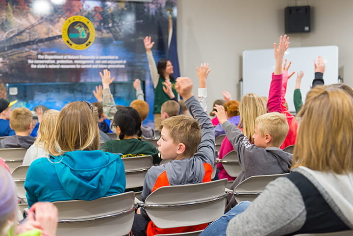 children in a classroom with arms raised from behind