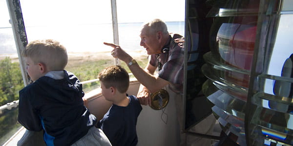 A man and children look out the windows at the water from the top of a lighthouse tower.