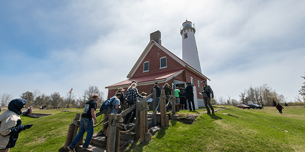 A group of people walking into Tawas Point Lighthouse for a tour.