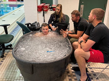 man sits in ice tank with people watching