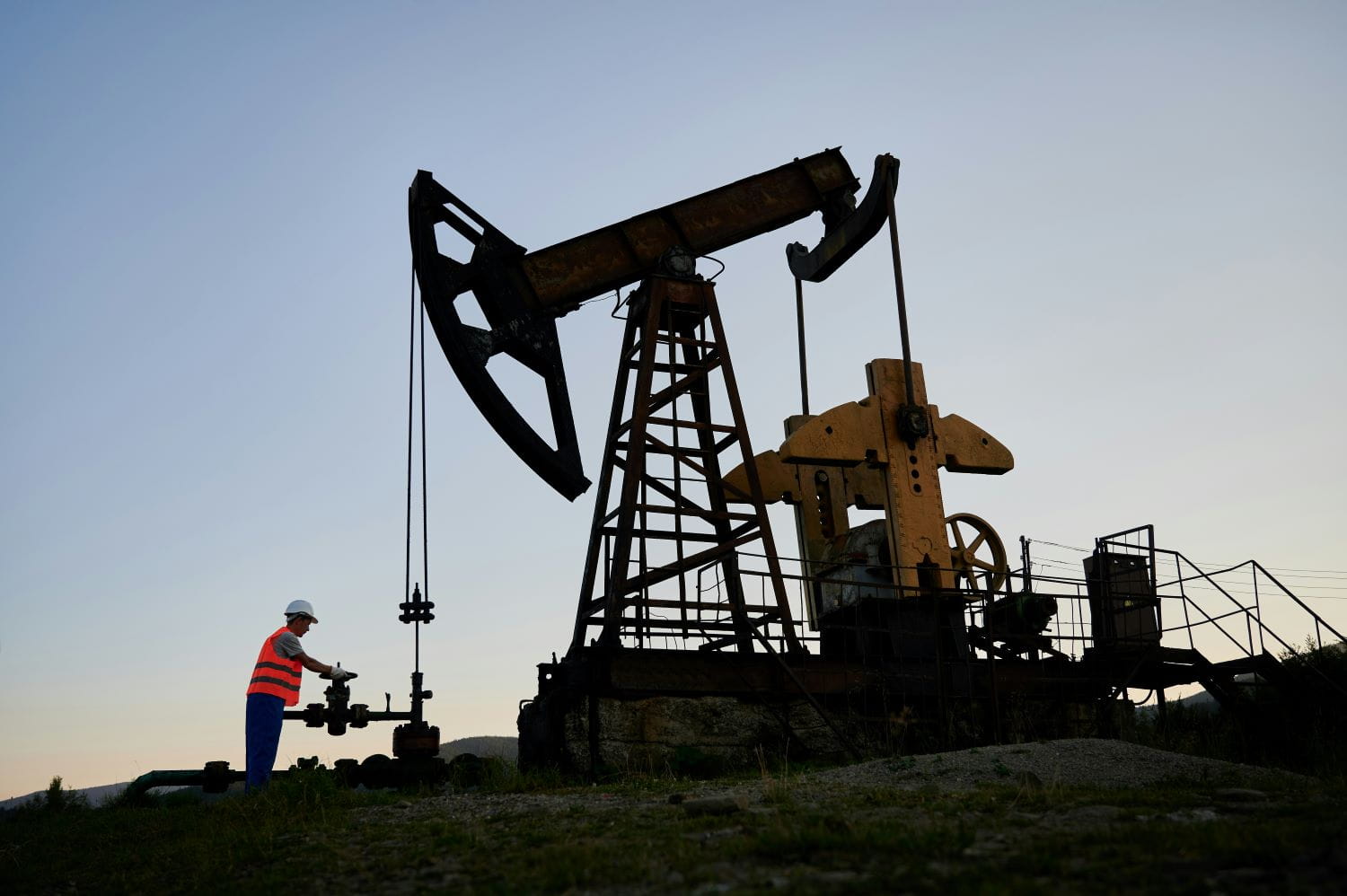 A worker adjusts something on an oil drill at sunset