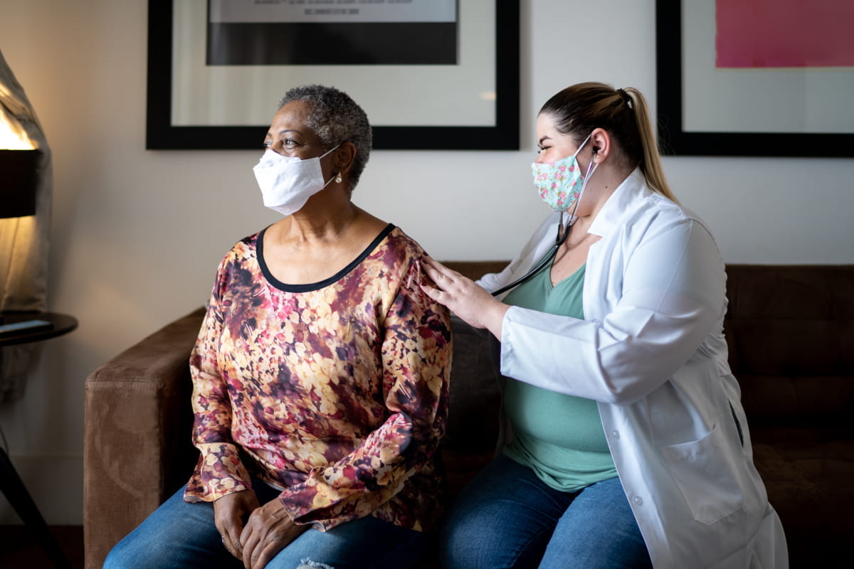 Younger female provider seated with stethoscope on back of seated older woman