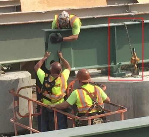 Construction workers on a bridge using a chain-down system to securely anchors a steel I-girder to the bridge substructure.