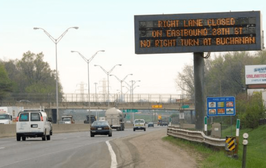 Dynamic message sign on highway providing traffic notice of lane closure ahead.