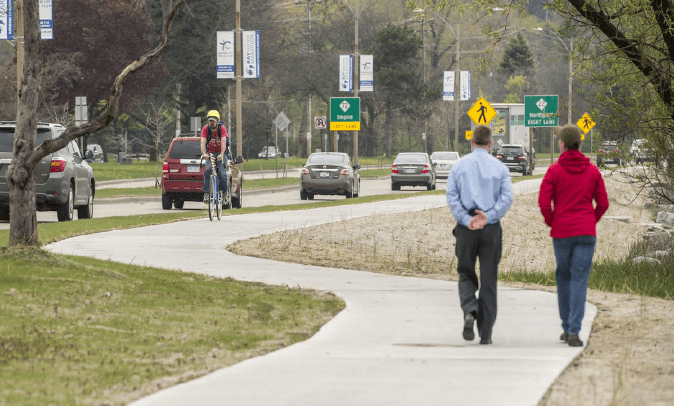 An image of pedestrians and a bicyclist using a paved path that runs along a city street.