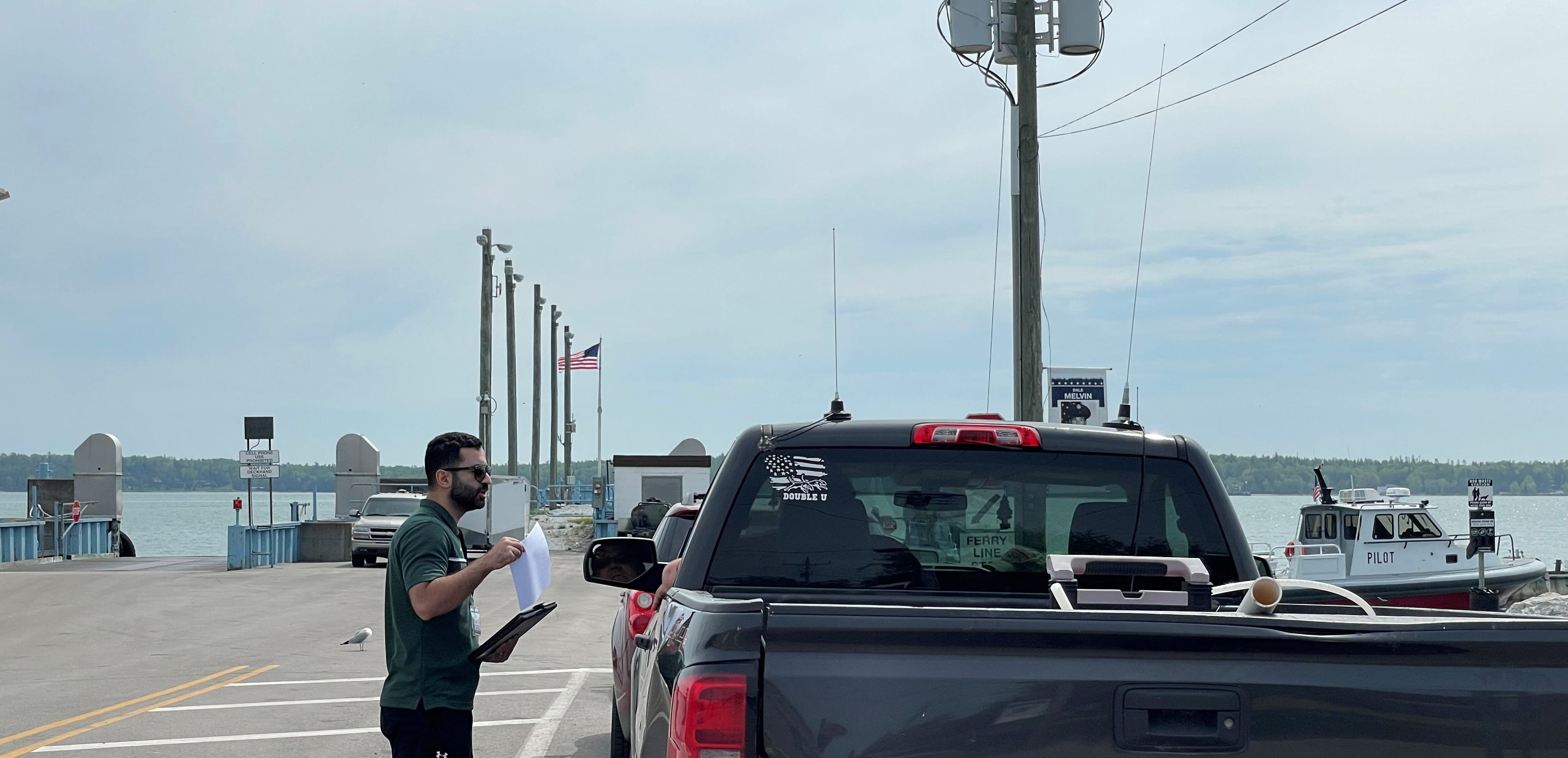 A vehicle approaching a ferry dock entrance, with a researcher holding out a survey questionnaire to the driver.