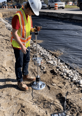 An MDOT worker holds a level against a retaining wall to measure tilt.