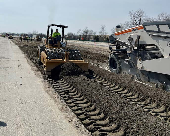 An MDOT worker holds a level against a retaining wall to measure tilt.