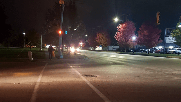 Partially or poorly lit intersection showing a pedestrian waiting to cross.