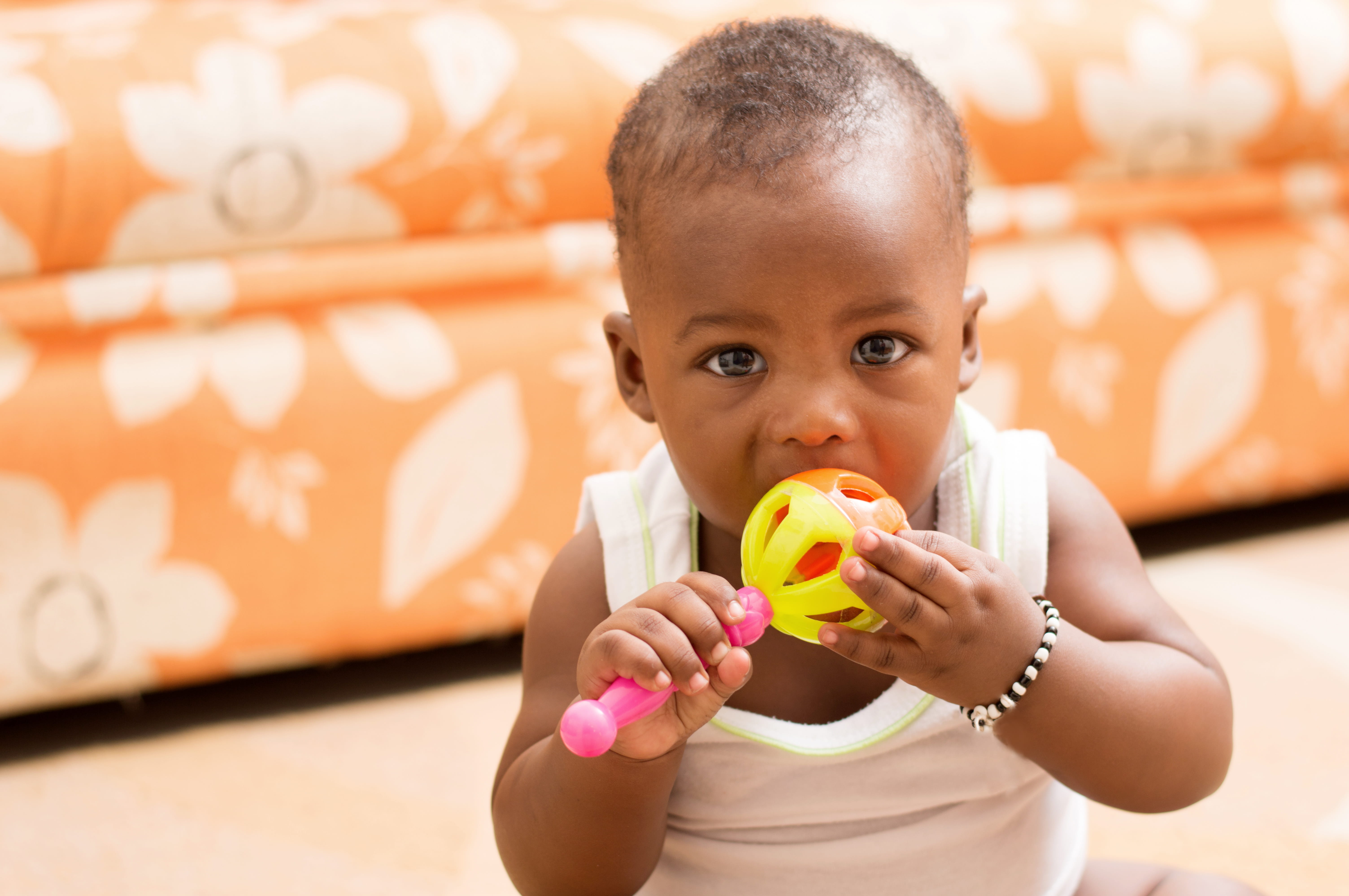 Toddler sitting down on floor and chewing on toy rattle