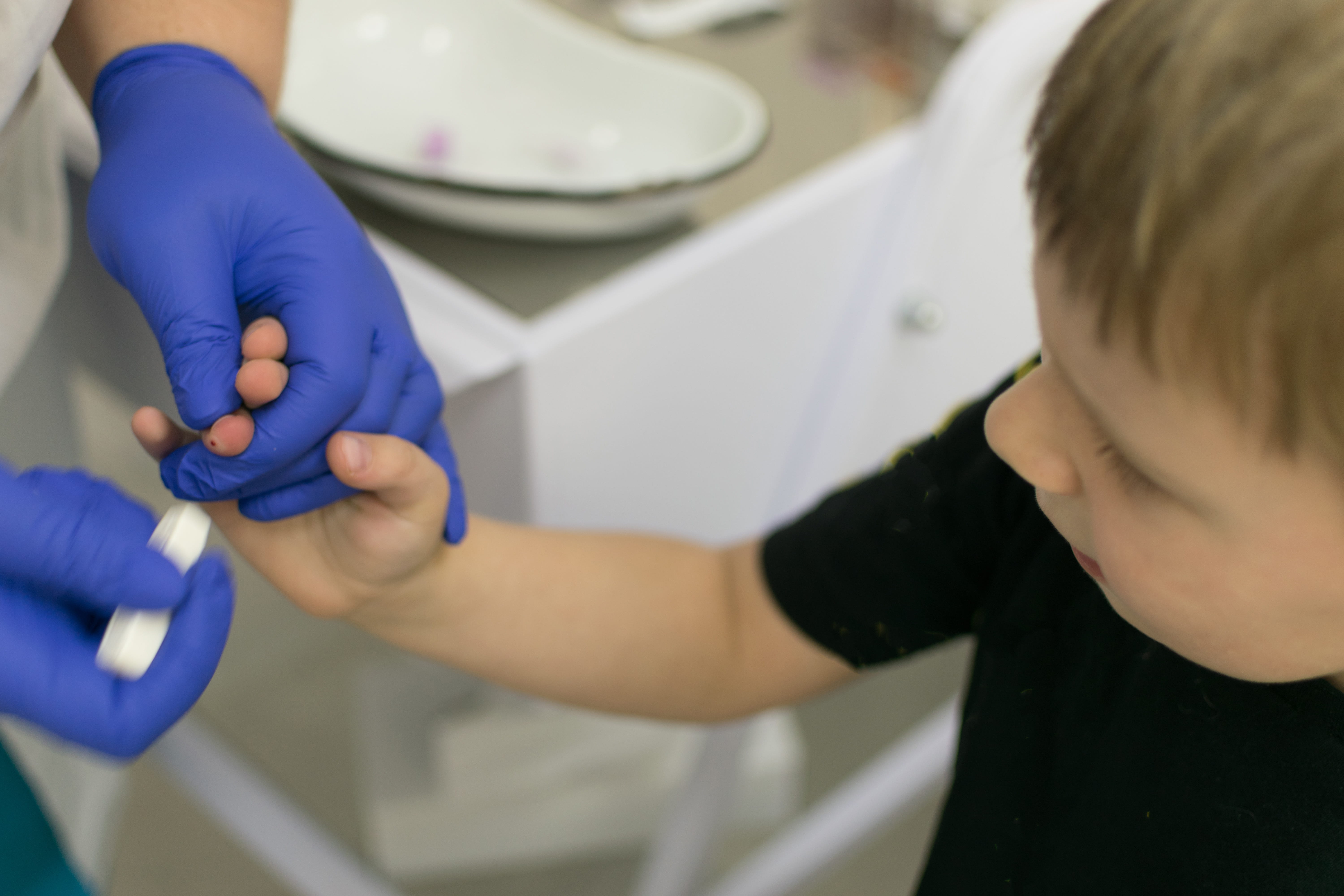 Healthcare provider wearing gloves to perform a blood lead test on a young boy