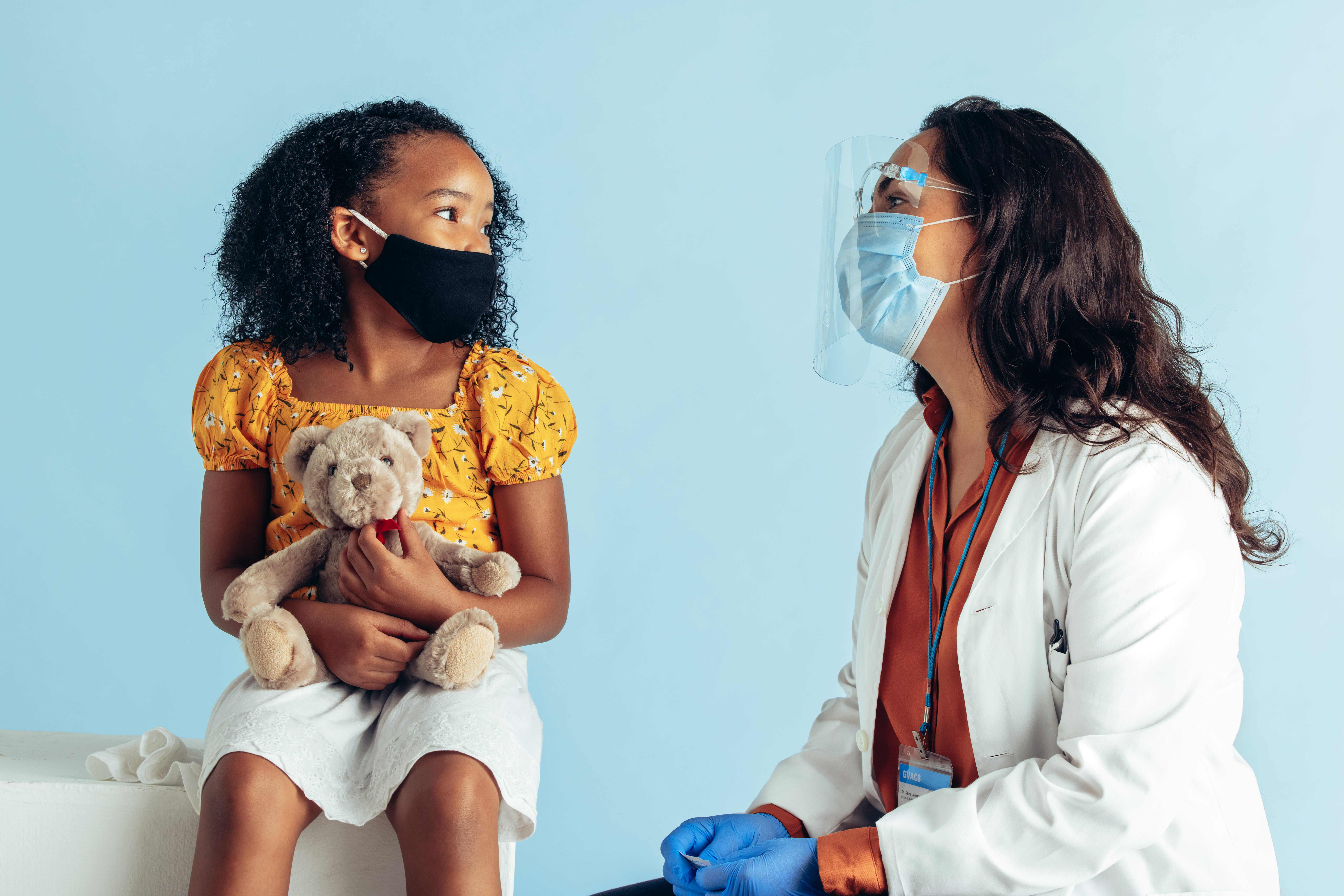 Young female child holding a teddy bear while talking with her healthcare provider