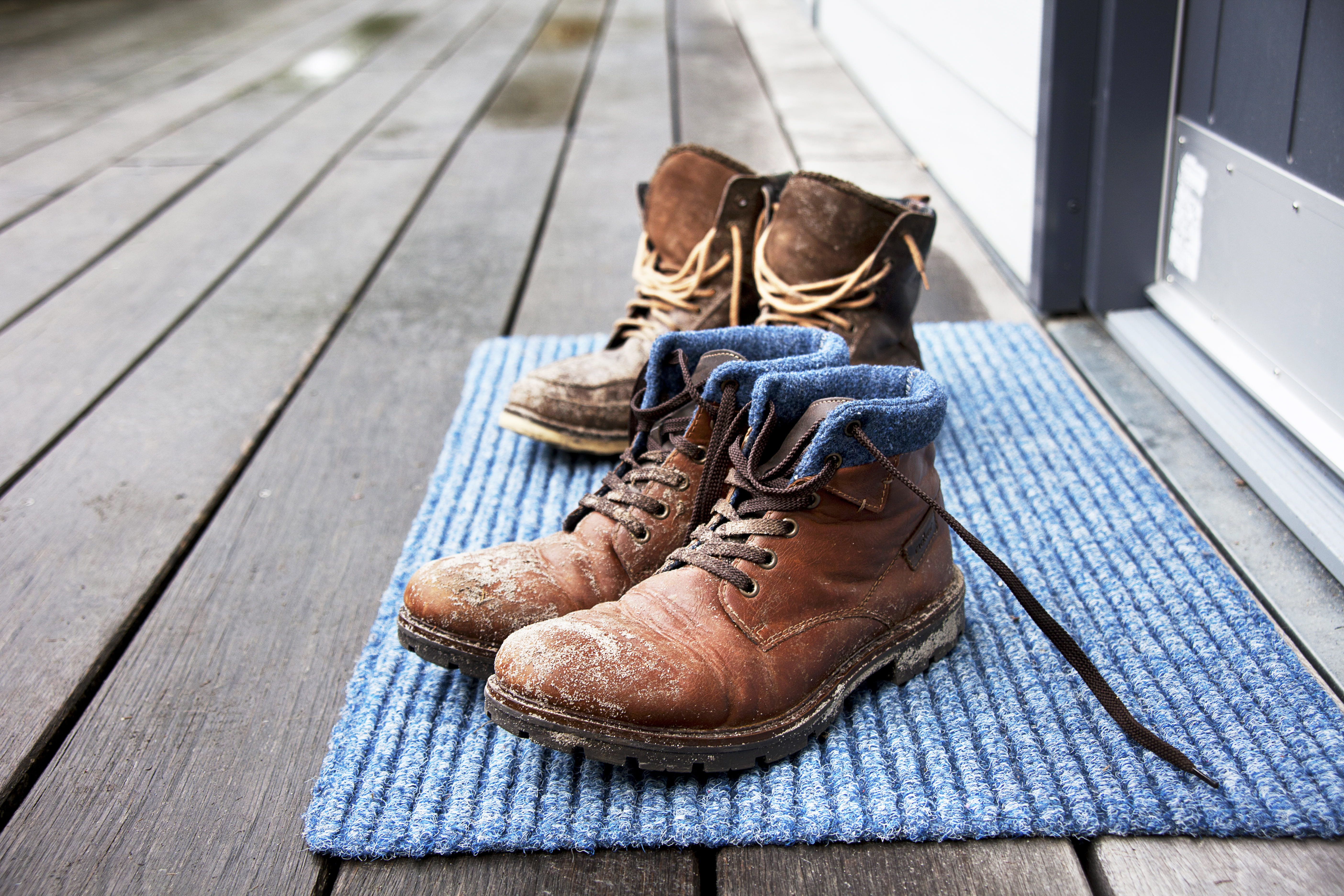 Two pairs of dirty work boots sitting on a floor mat outside of home