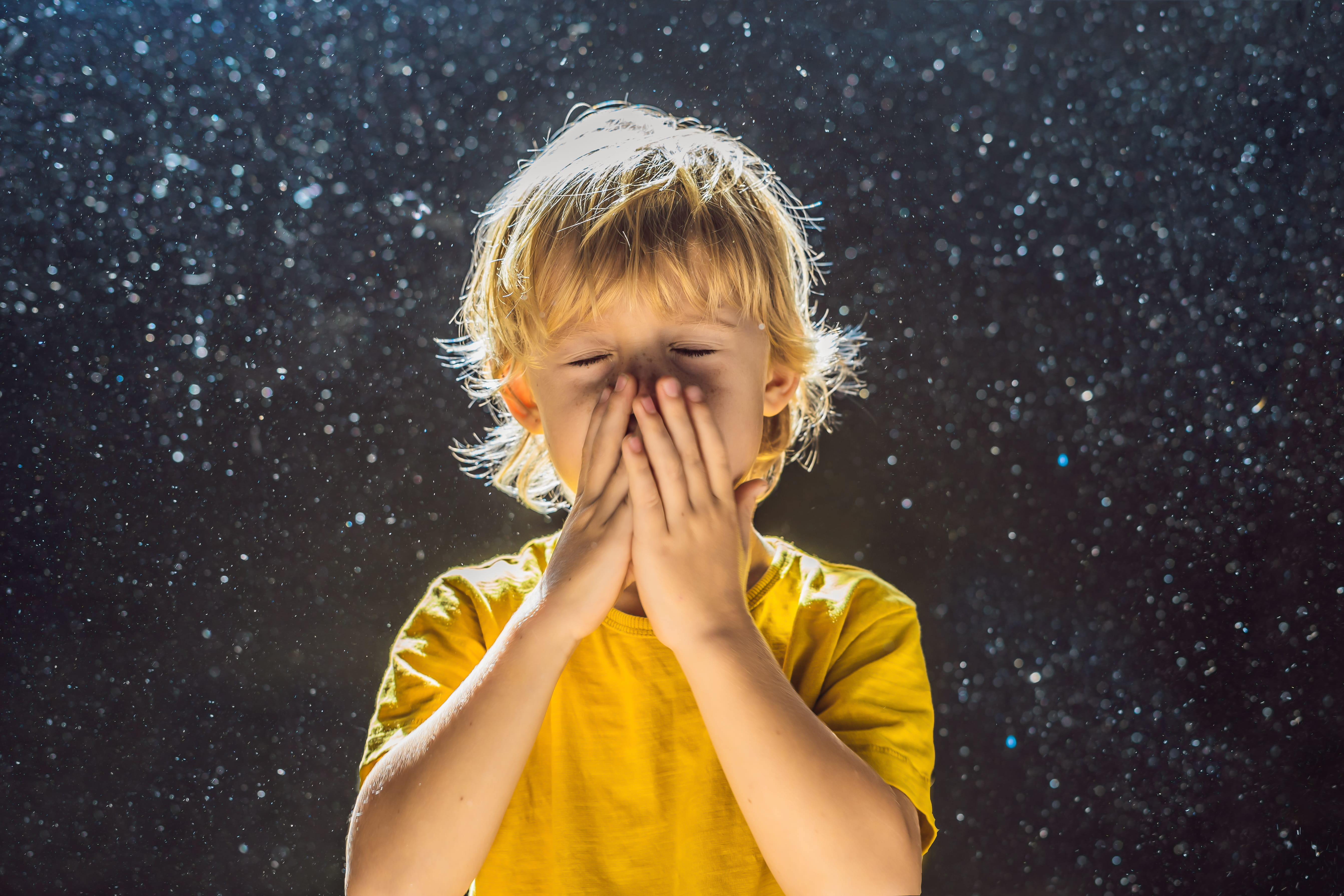 Young boy holding hands over his mouth as dust floats around him