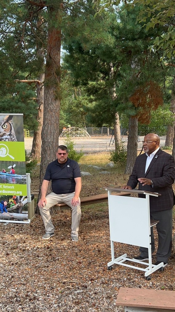 Rawlan Lillard II speaking at a podium outdoors in front of attendees at an event.