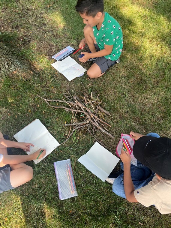 Aerial view of three children sitting on the grass working on an activity