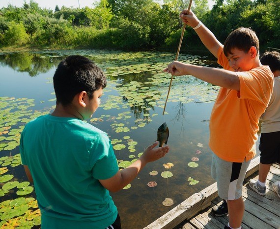 Two kids on a bridge at the lake retrieving a fish from a fishing pole