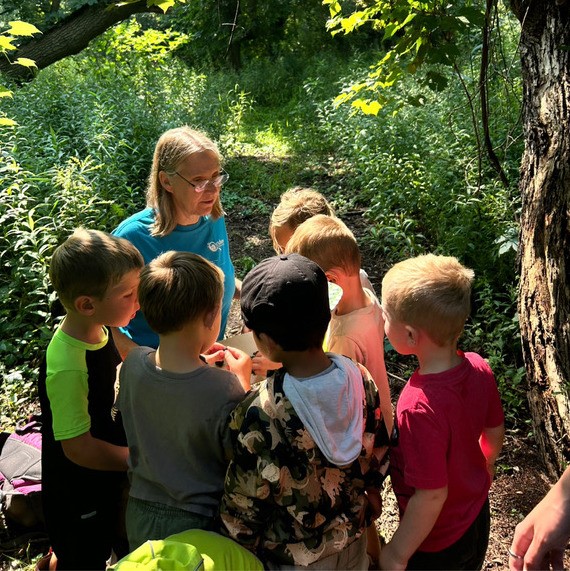 A group of children gathered around a teacher in the woods
