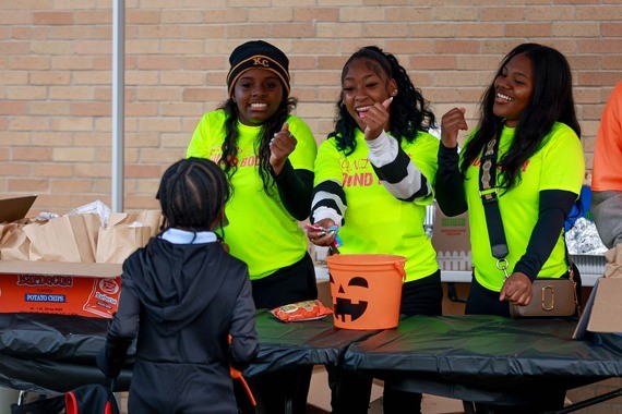 Three older students in neon green shirts guide and smile with an elementary student during a Lights On Afterschool event