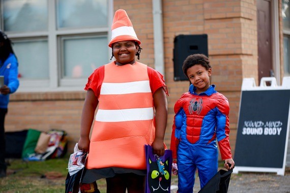 Two boys smiling at the camera, one dressed as Superman and the other wearing a traffic cone costume, during a Lights On Afterschool Day event