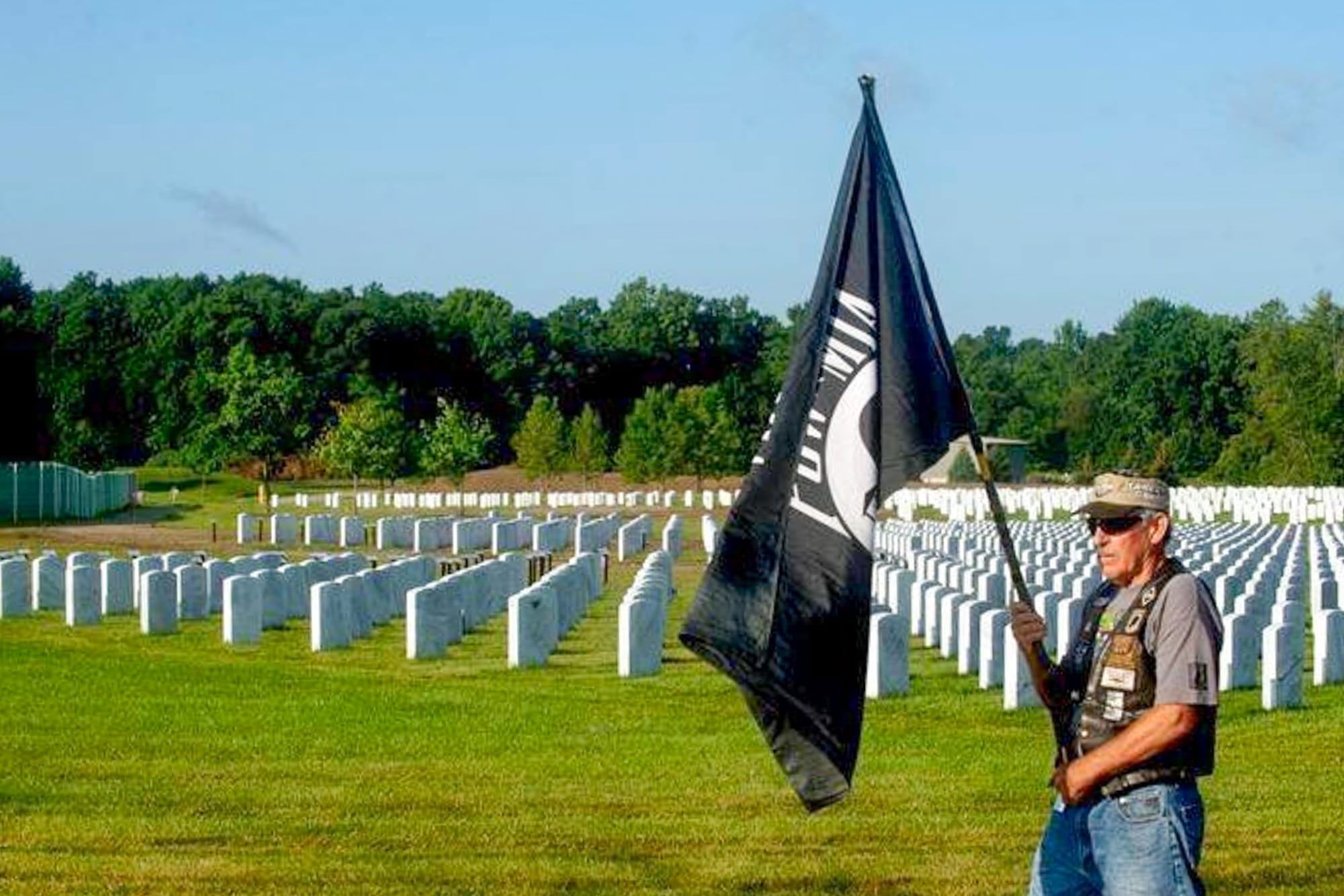 light-skinned man holding pow flag in cemetery