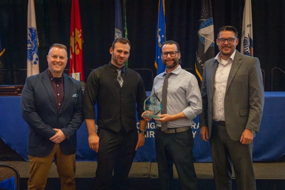 four light skinned men on stage with one man holding a crystal award