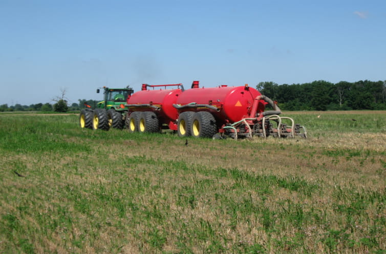 A tractor hauling a bright red tank through a farm field applying biosolids