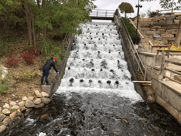 an egle employee stands near an outpouring of water, collecting a sample