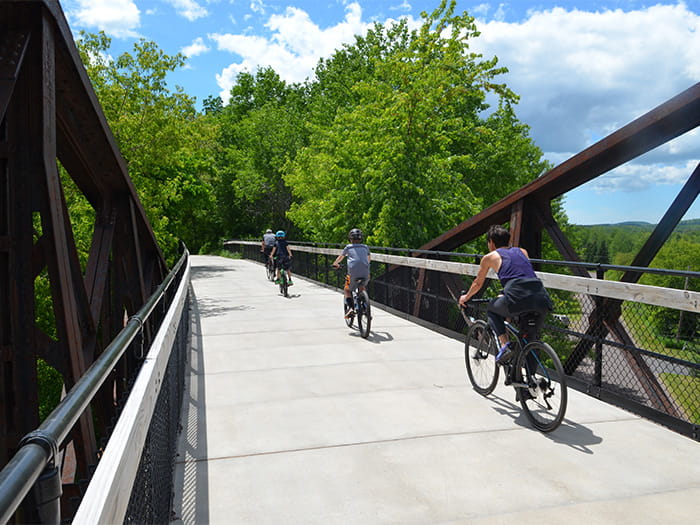 three people riding bikes over pedestrian trail bridge